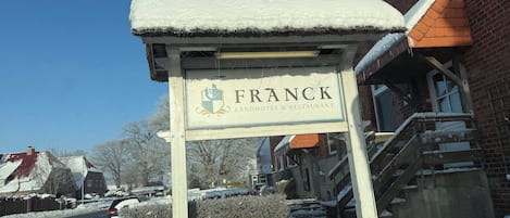 A snow-covered sign for Franck Hotel & Restaurant with a brick building in the background.