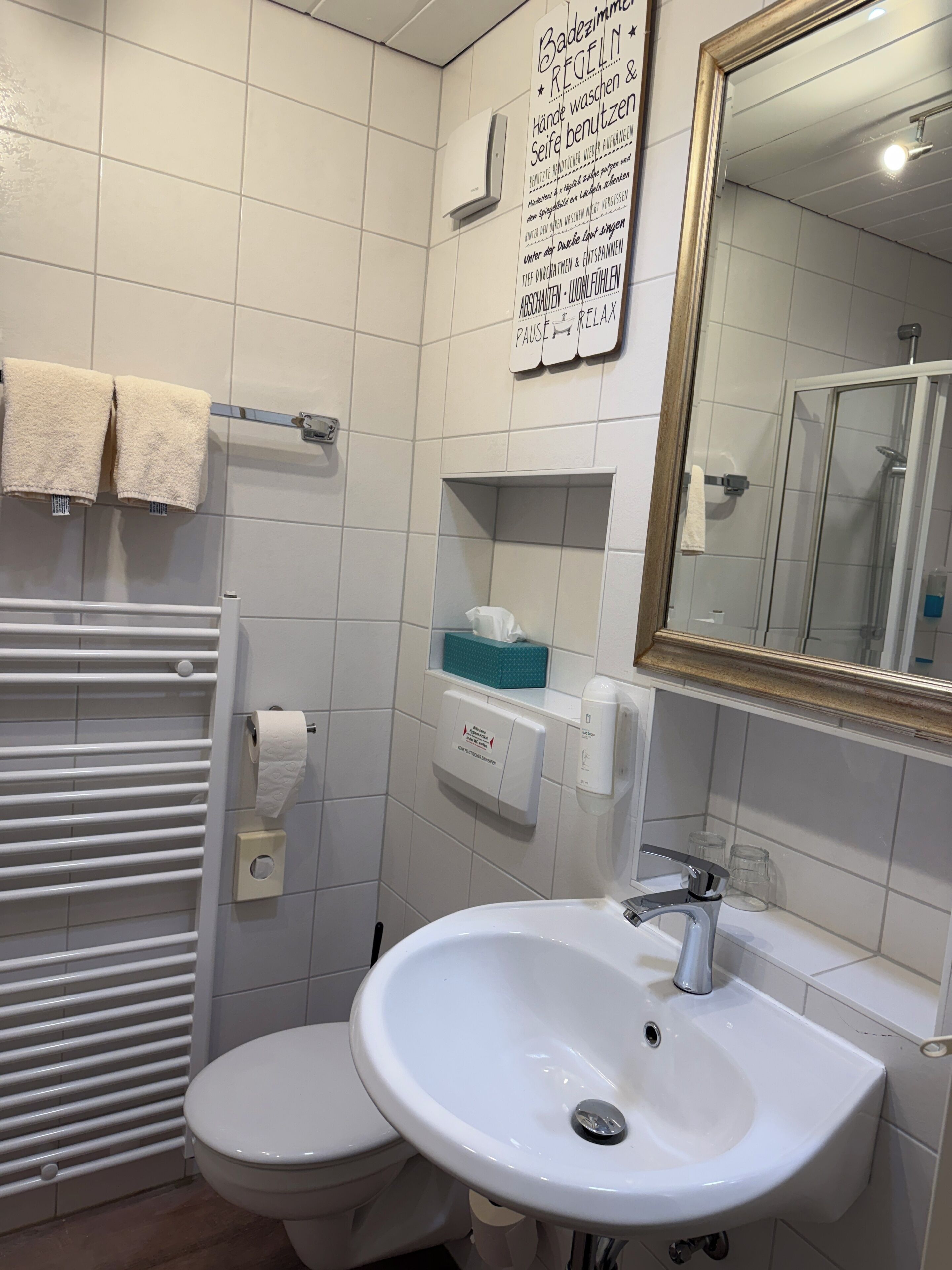 A bathroom with a toilet, a sink, a towel rack, a mirror, and a sign with instructions.