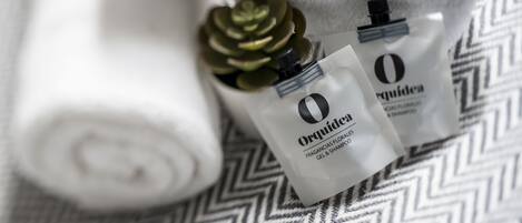 A rolled white towel and two bottles of Orquidea fragrance and shampoo on a patterned fabric.