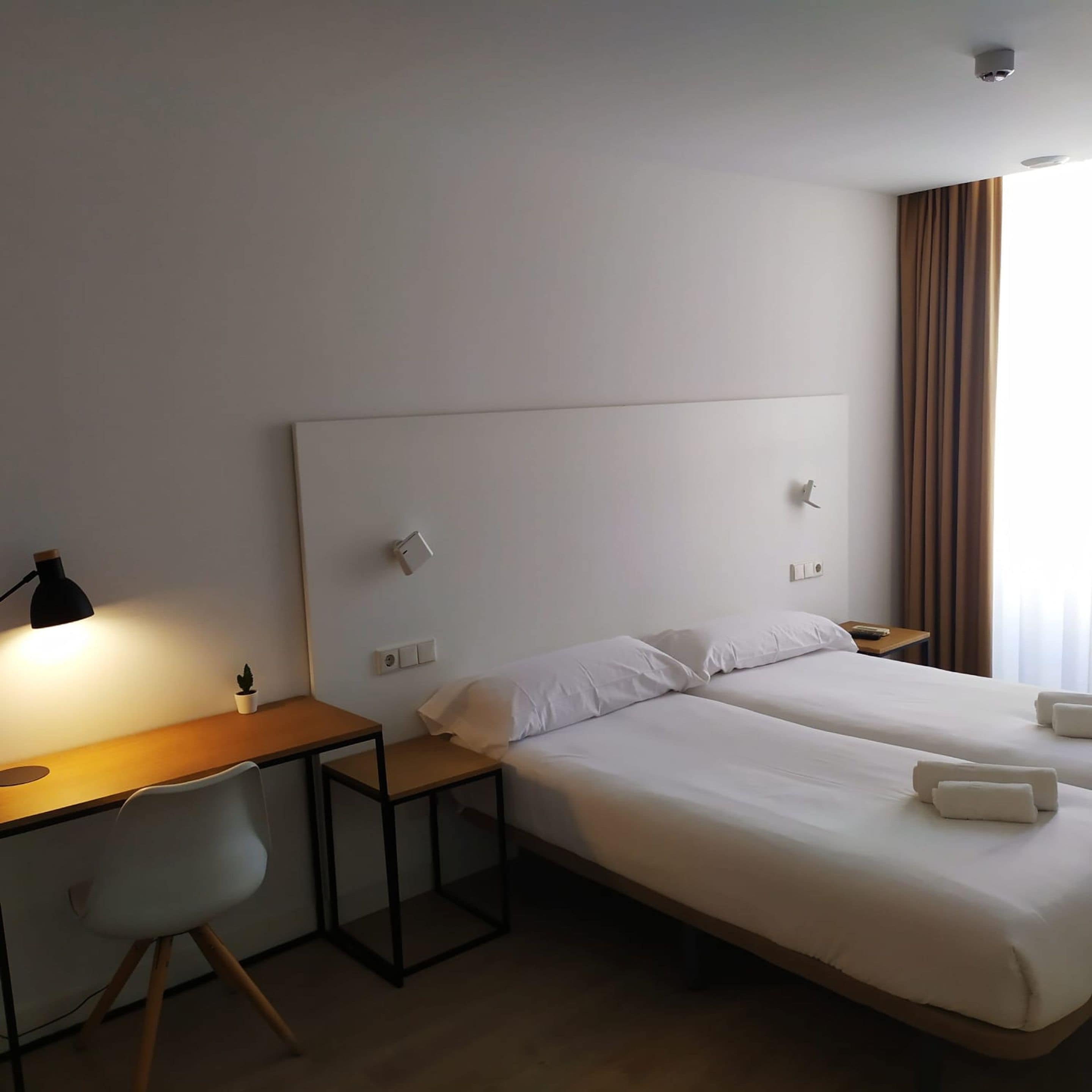 Ein Hotelzimmer mit zwei Betten, einem Schreibtisch, einem Stuhl und einer Lampe.