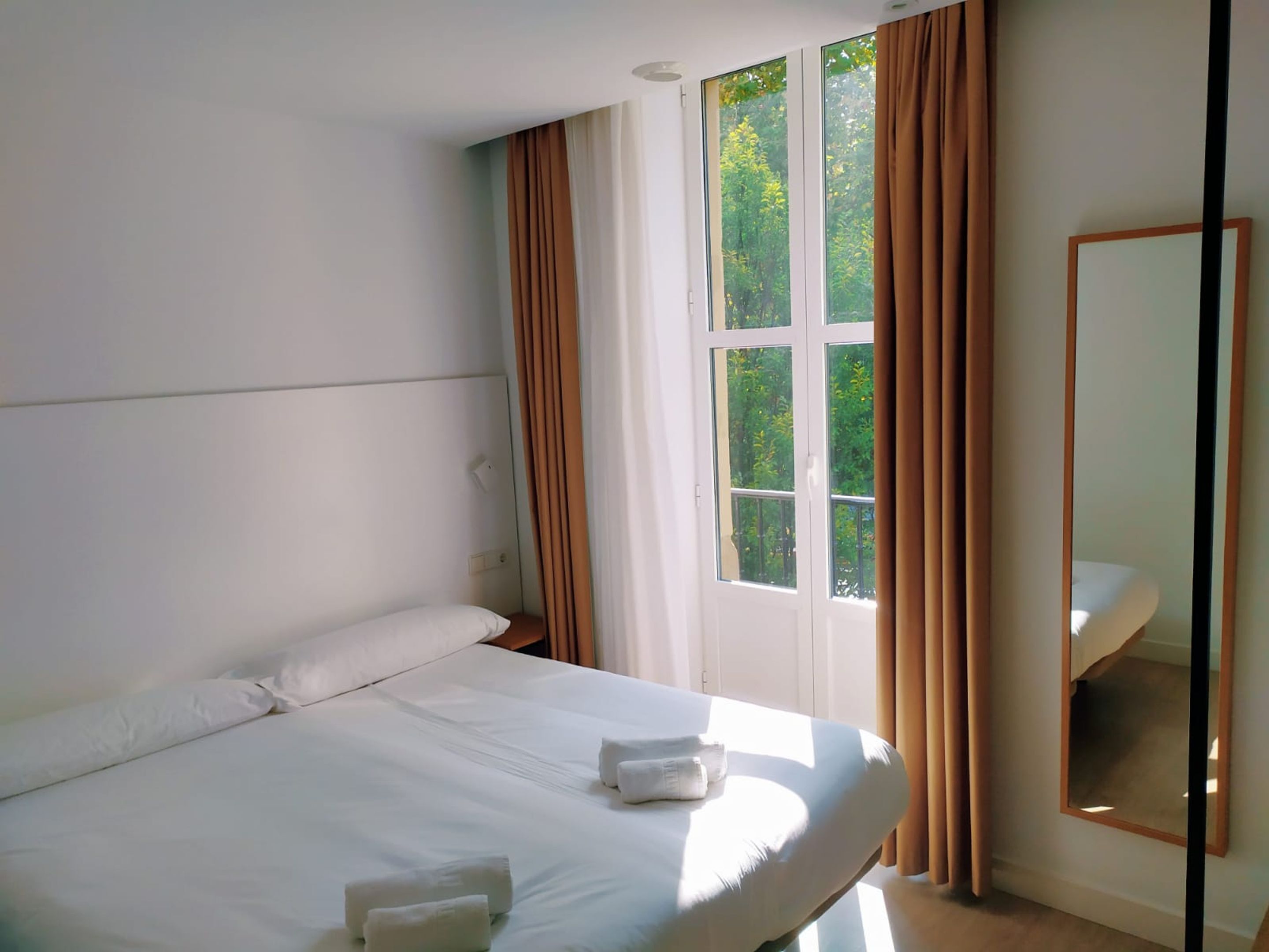 Een hotelkamer met een bed, een raam met gordijnen en een spiegel aan de muur.