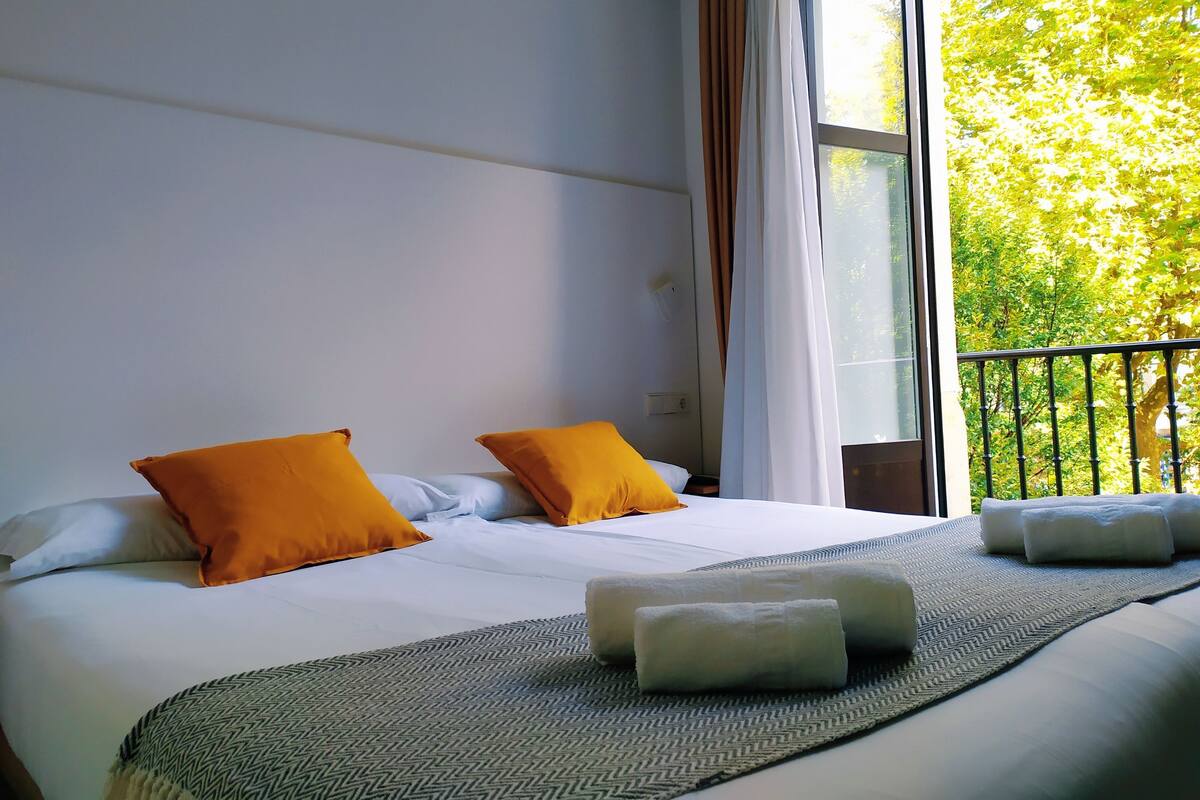 Une chambre d’hôtel avec un grand lit, deux oreillers, une couverture et une vue sur les arbres par la fenêtre.
