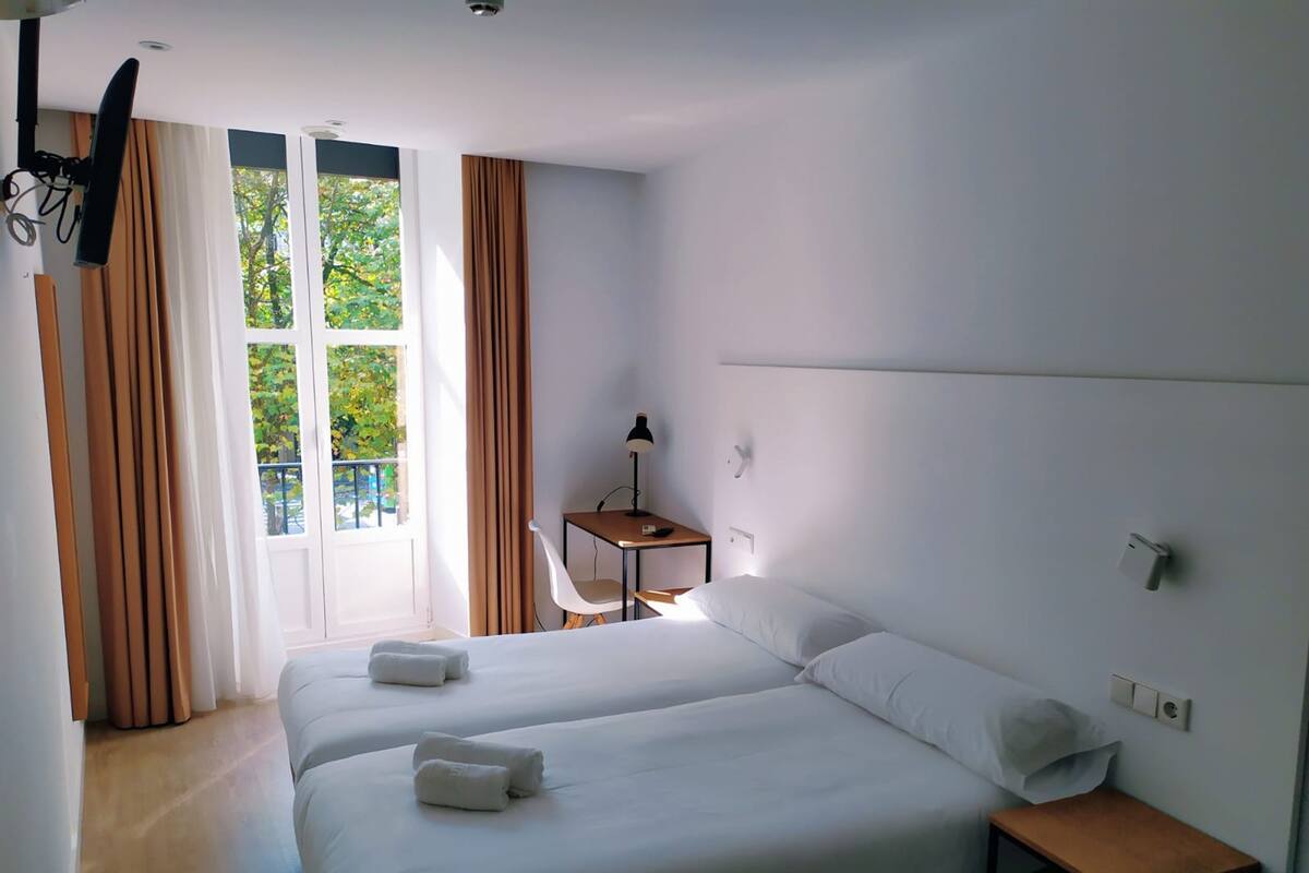 Une chambre d’hôtel avec deux lits, un bureau, une chaise et une fenêtre avec des rideaux.