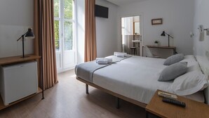 A modern hotel room with a bed, a desk, a television, and a small refrigerator. - Pensión Sarriegi (San Sebastián)