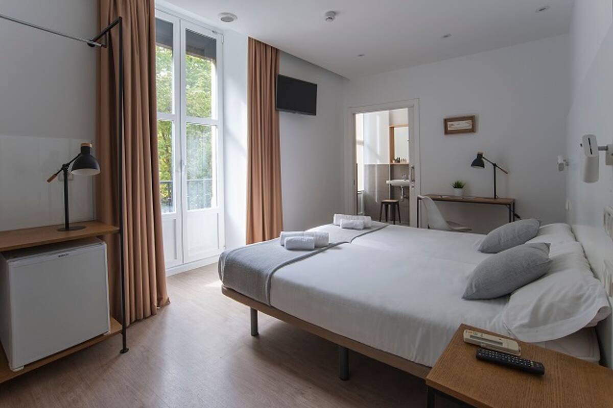 Une chambre d’hôtel moderne équipée d’un lit, d’un bureau, d’une télévision et d’un petit réfrigérateur.