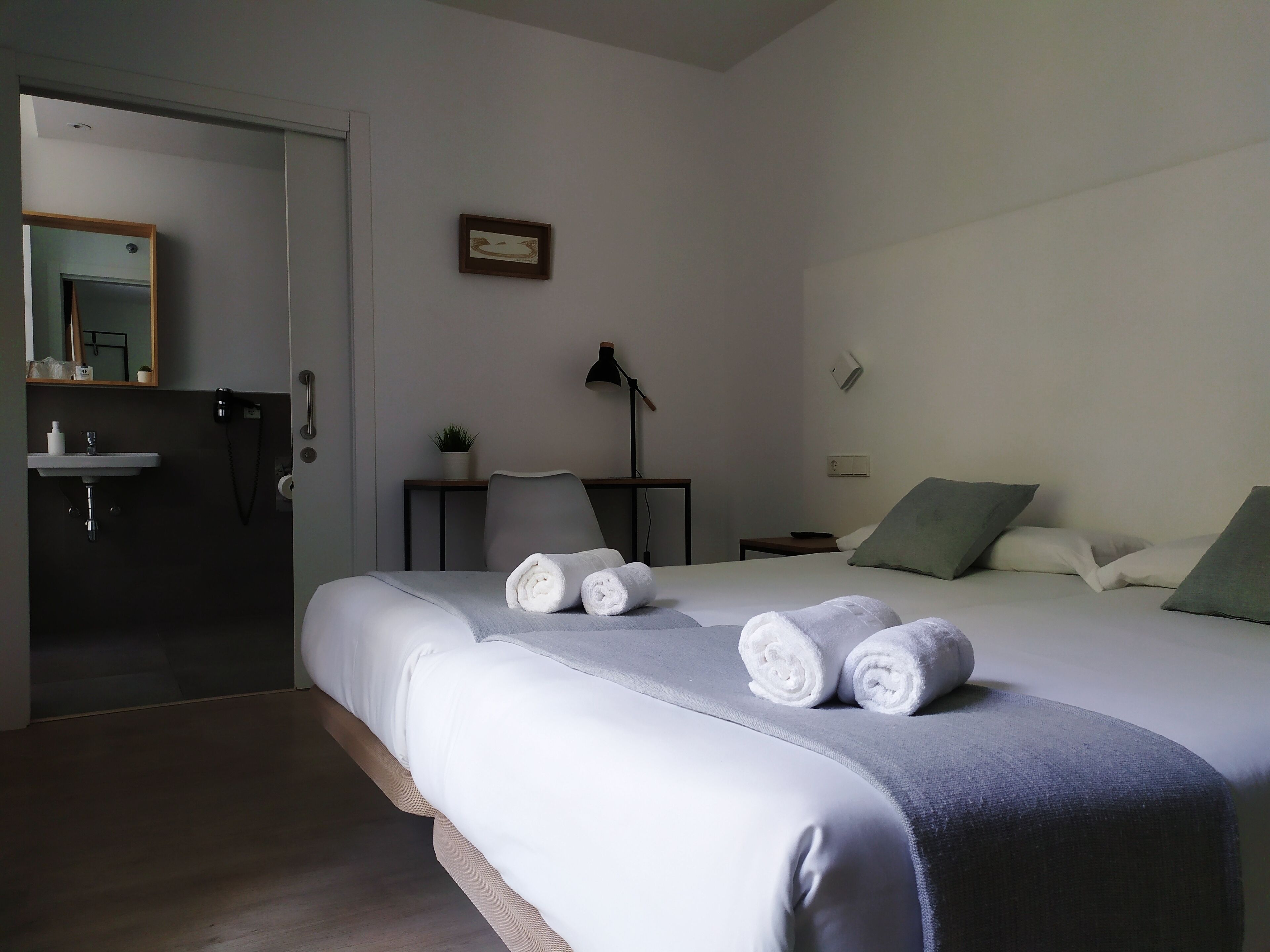 A bedroom with a bed, a bedside table, a lamp, a wall-mounted air conditioner, and a small potted plant.