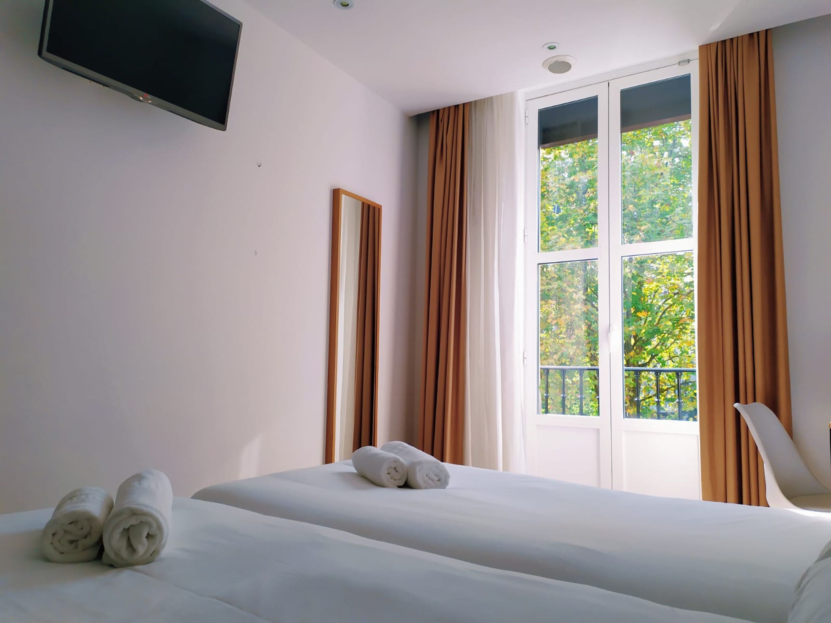 A hotel room with a large bed, a flat-screen TV mounted on the wall, and a window with curtains.