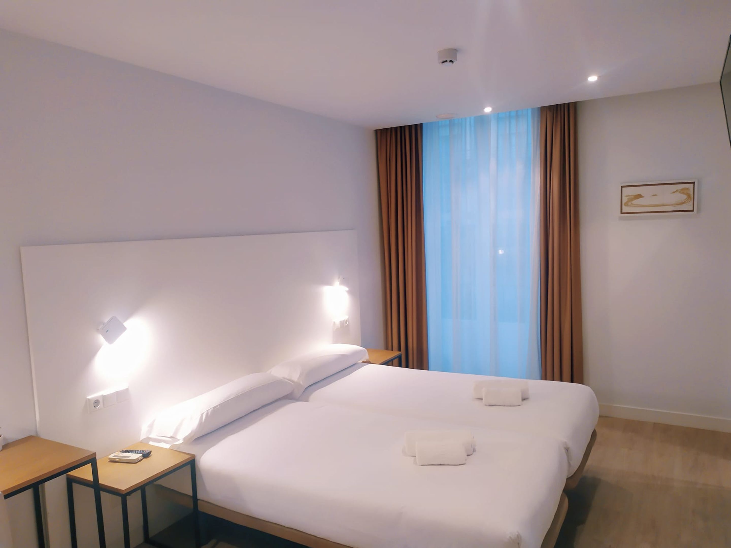 Una habitación de hotel con una cama grande, dos mesitas de noche y una ventana con cortinas.