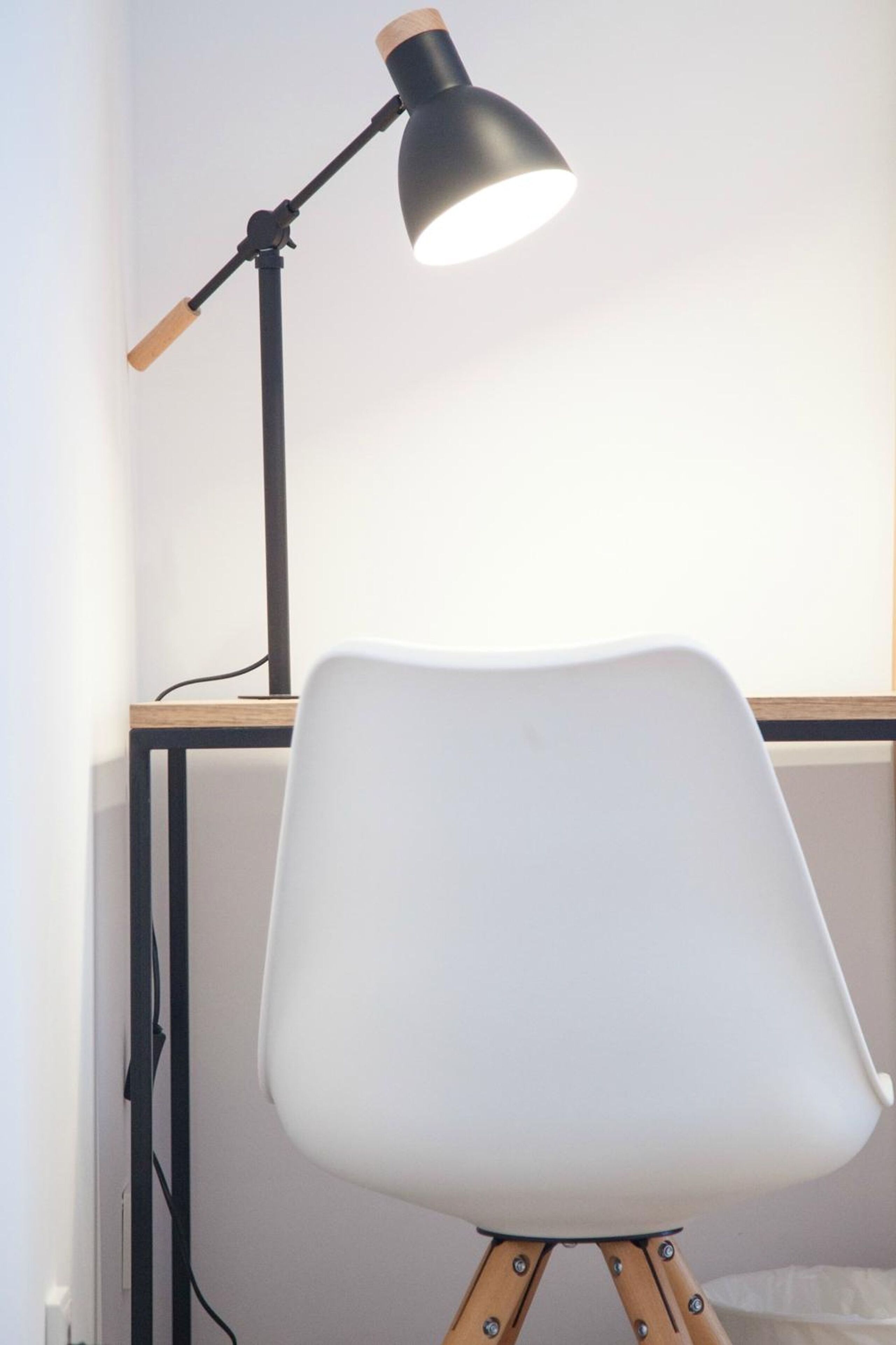 Una silla blanca con patas de madera y una lámpara de escritorio negra con mango de madera.