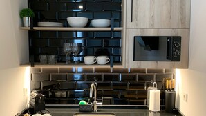 A modern kitchen with a black backsplash, wooden cabinets, a stainless steel sink, and a microwave. - Pensión Sarriegi (San Sebastián)