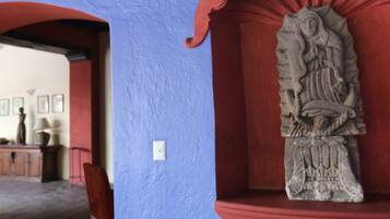 Una estatua de piedra en un nicho con un marco rojo, una pared azul y una puerta que da a una habitación con un escritorio y una lámpara.