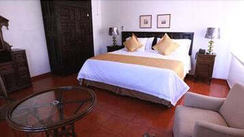 A hotel room with a bed, a wooden dresser, a glass table, and a chair.