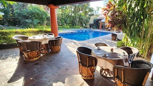 An outdoor patio with a pool, wicker furniture, and a view of the surrounding greenery.