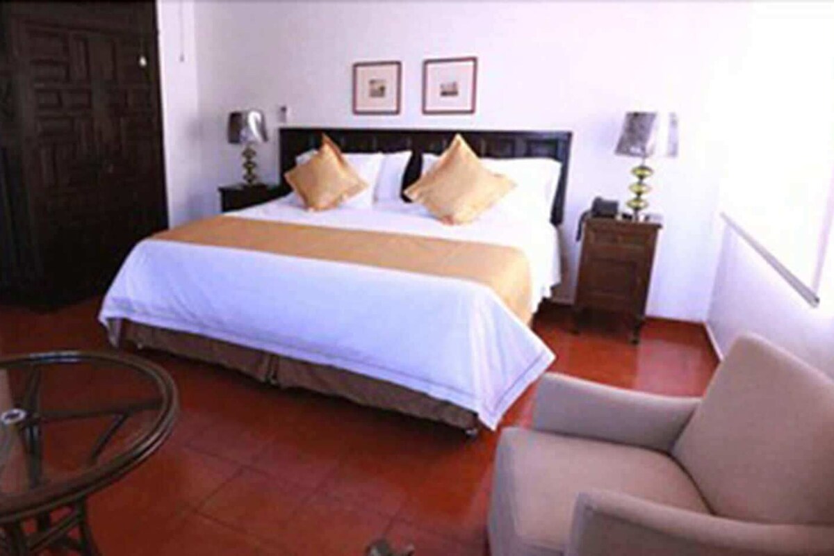 A hotel room with a bed, a chair, a table, and a wooden cabinet.