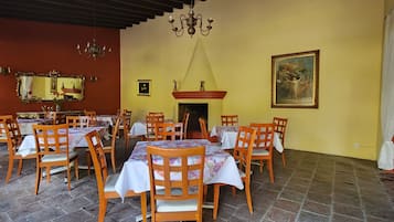 Un comedor con varias mesas y sillas, un candelabro, una chimenea y un cuadro grande enmarcado en la pared.