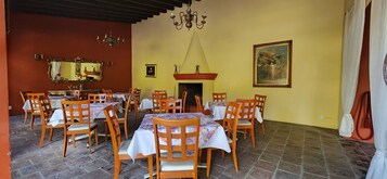 Un comedor con varias mesas y sillas, un candelabro, una chimenea y un cuadro grande enmarcado en la pared.