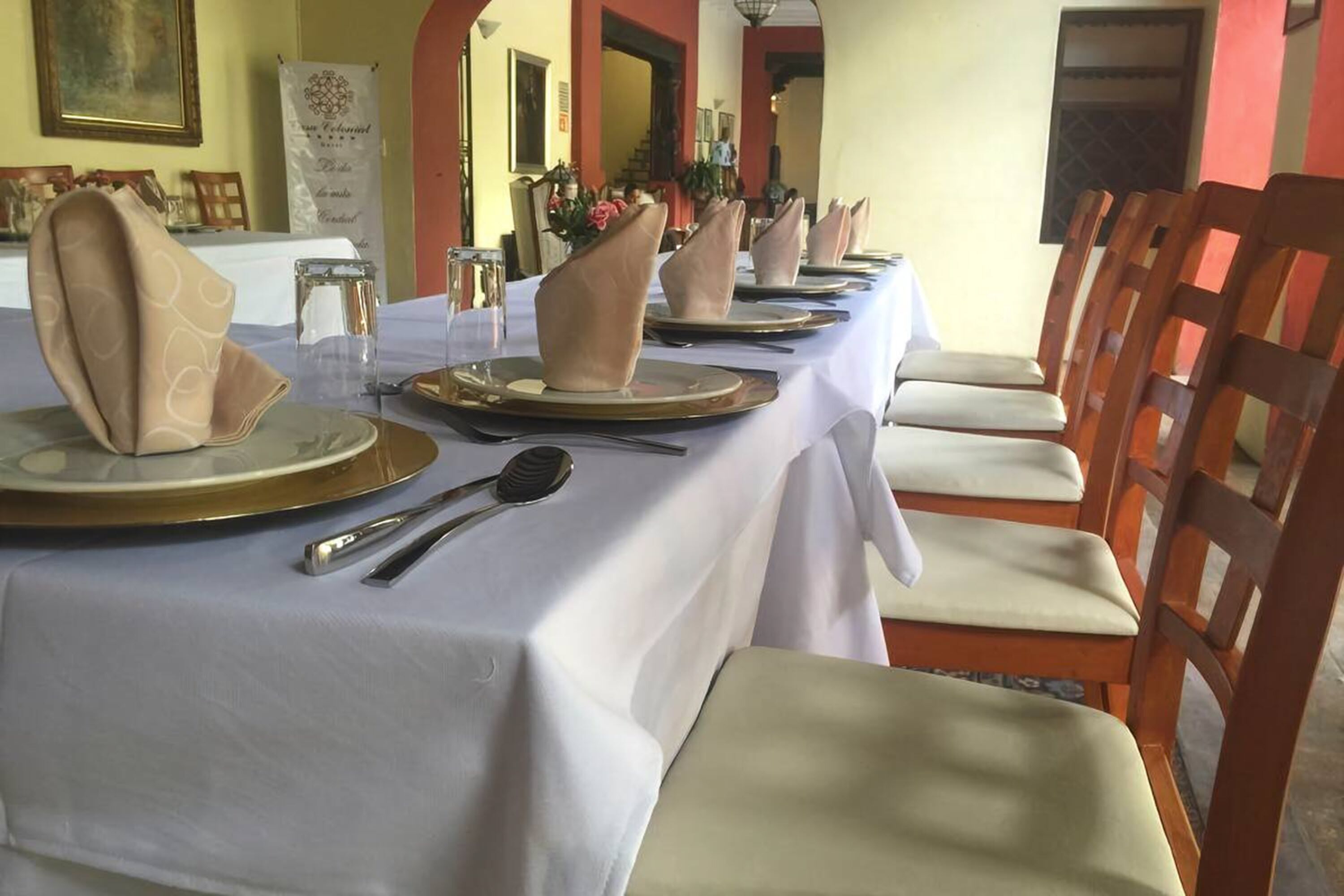 A dining table set with white tablecloths, gold plates, and beige napkins.