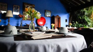 A dining table set with white tableware and a vase of flowers, with a blue wall and framed pictures in the background.