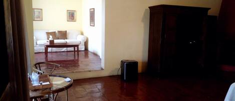 Una habitación con piso de madera, un sofá blanco, una mesita, un armario y una silla.