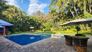A swimming pool surrounded by lush greenery and outdoor seating with umbrellas.