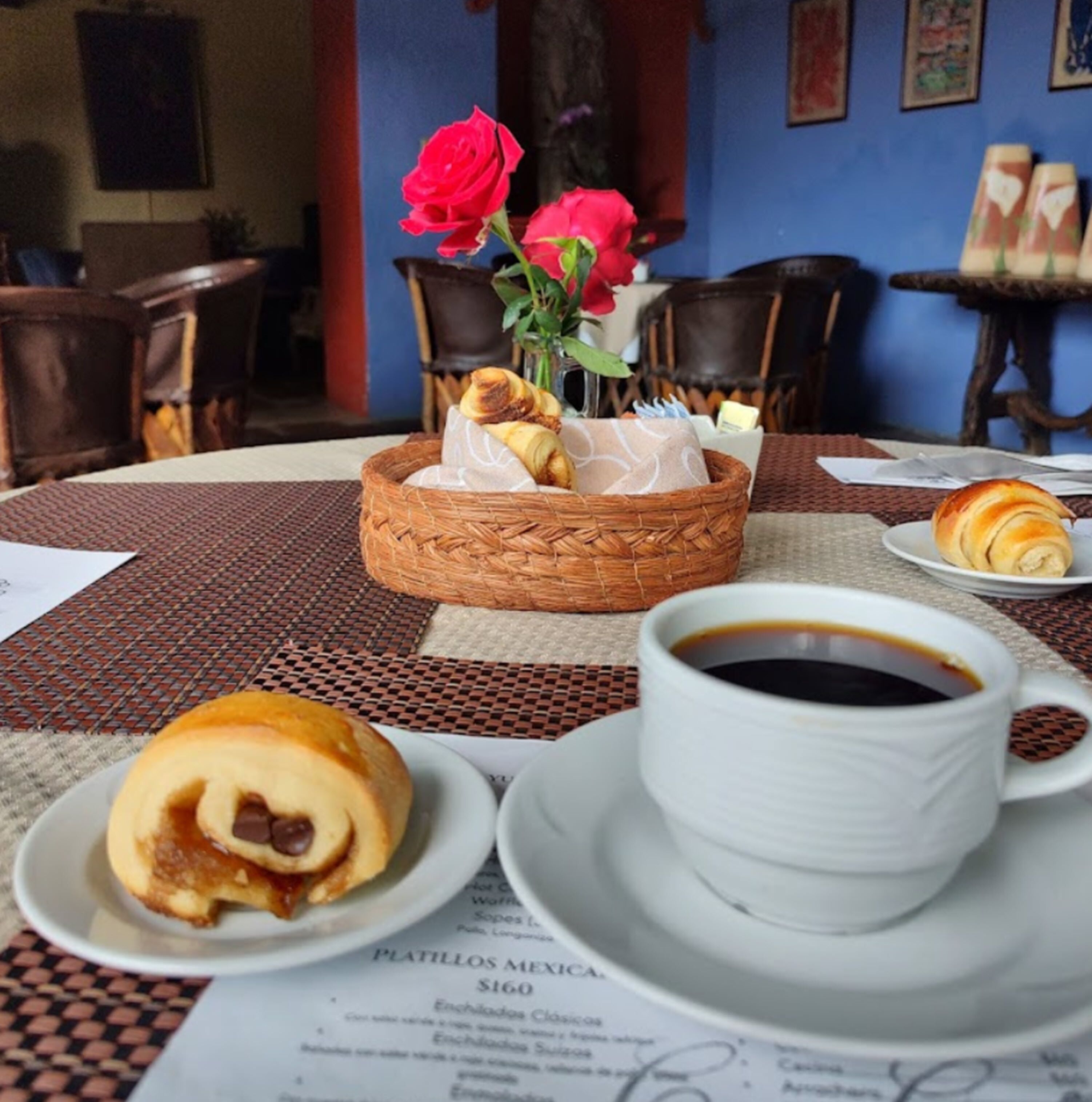 Una mesa de comedor con una cesta de pasteles, una taza de café y un plato con un croissant.