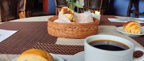 Una mesa de comedor con una cesta de pasteles, una taza de café y un plato con un croissant.