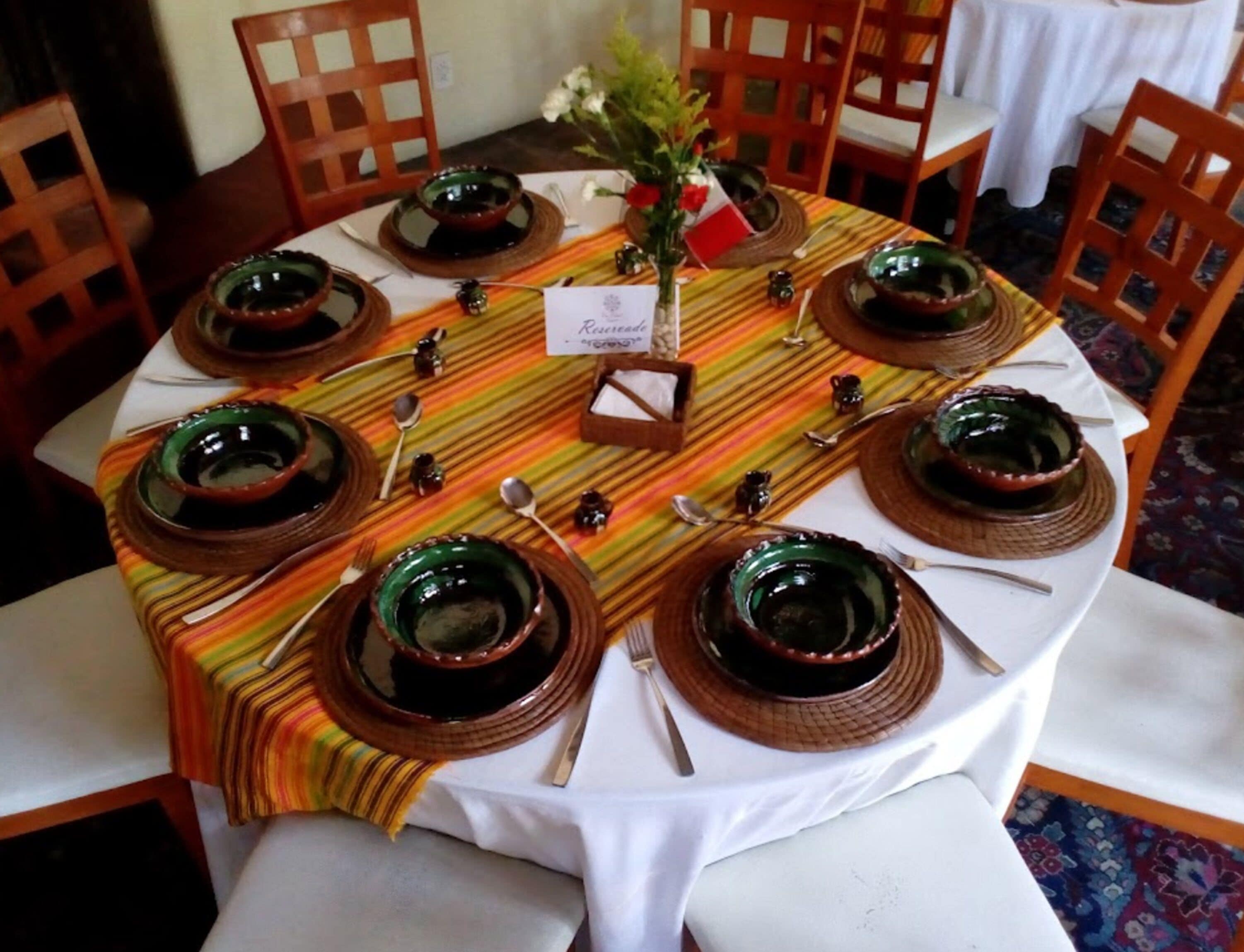 Una mesa redonda de comedor con una colorida mantel individual, rodeada de sillas de madera.