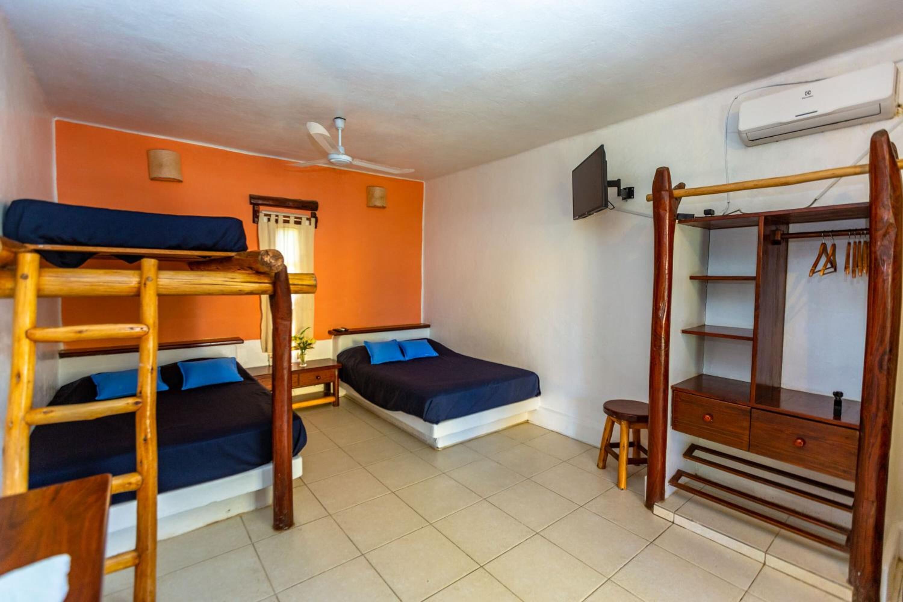 A dormitory room with bunk beds, a desk, a chair, a wardrobe, and a ceiling fan.