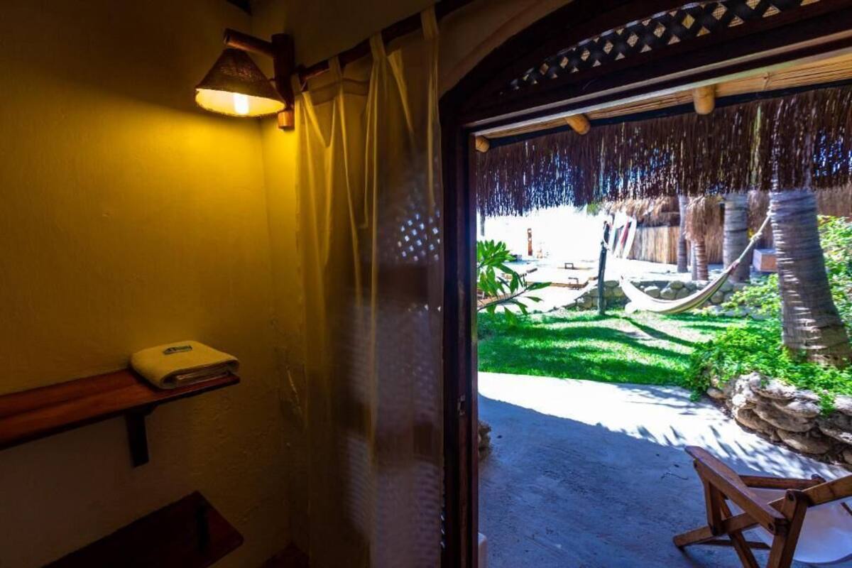 A doorway leading to a hammock and a thatched roof structure, with a shelf holding a white object and a lamp on the wall.