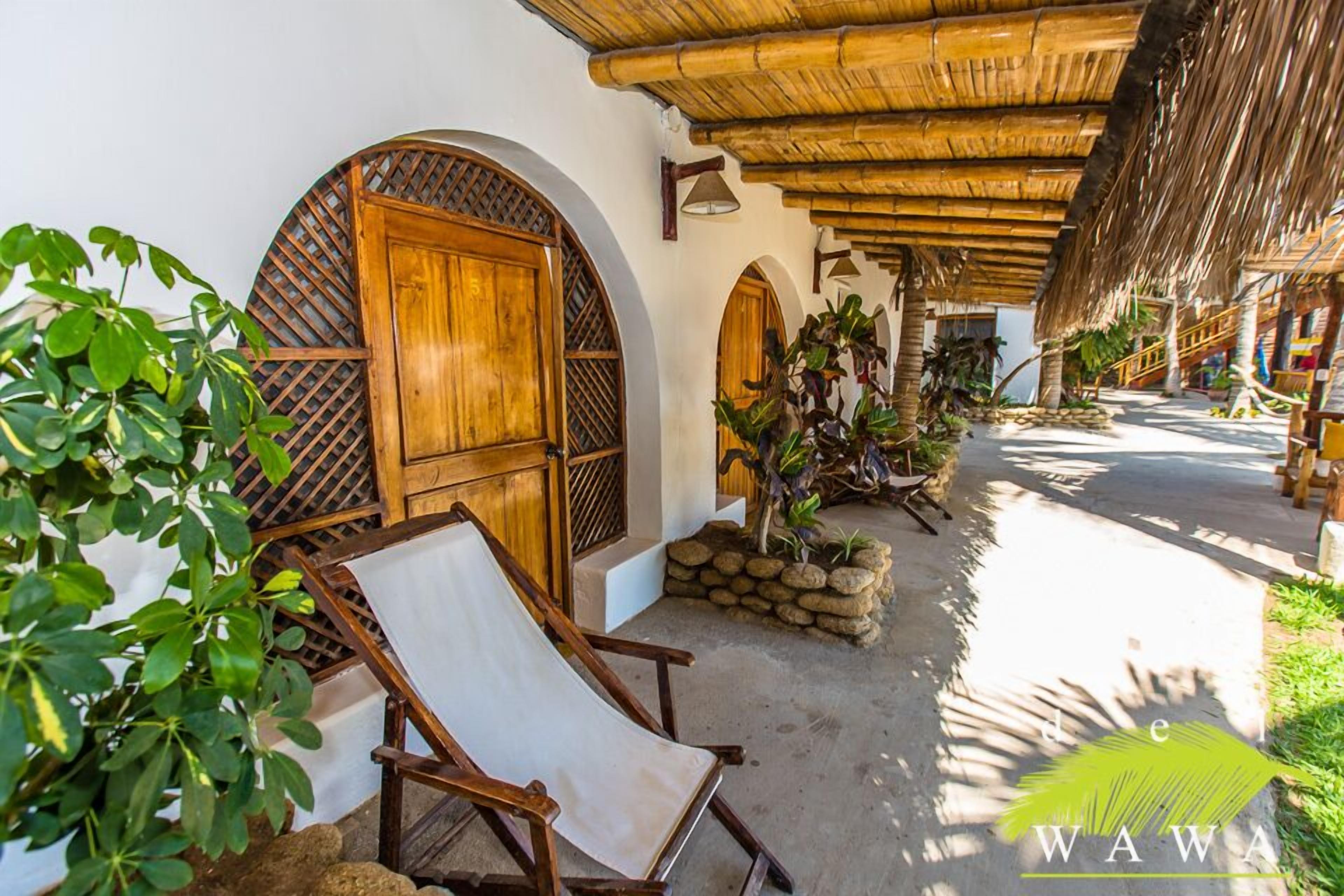 A covered outdoor area with a wooden door, a white chair, and potted plants.