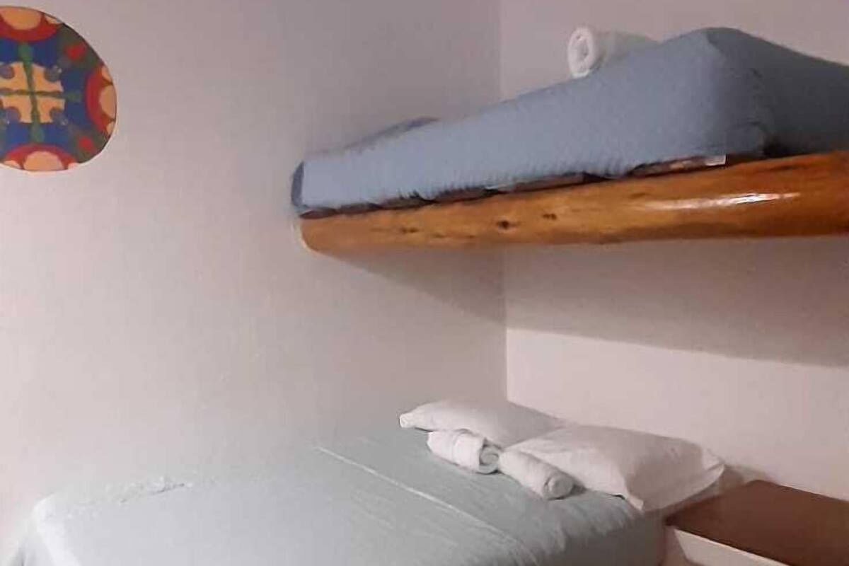 A small, compact room with a bunk bed and a single bed. The room has a wooden ceiling and walls with decorative circular patterns.