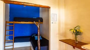 A room with a bunk bed, a ladder, a wooden bench, a small table with a vase, and a hanging light fixture.
