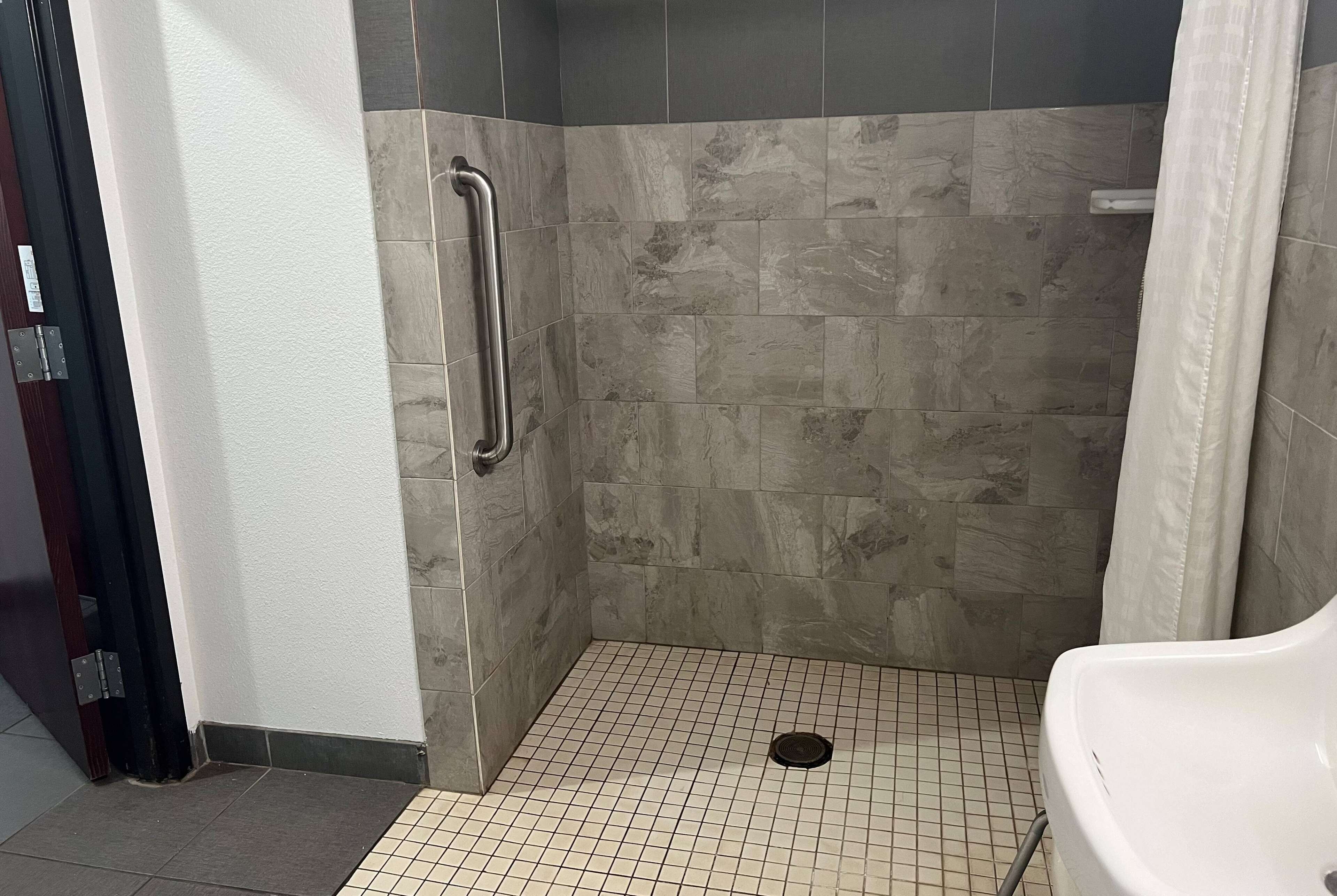 Un área de ducha pequeña con azulejos, un pasamanos, un lavabo blanco y piso de azulejos.