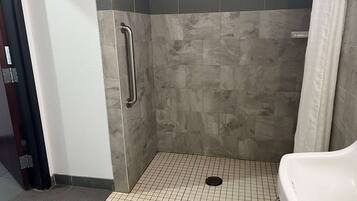 Un área de ducha pequeña con azulejos, un pasamanos, un lavabo blanco y piso de azulejos.