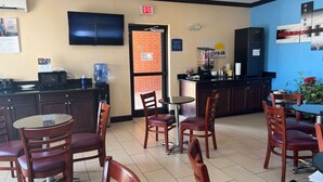 A restaurant with a kitchen area, a dining area with wooden chairs and a table, and an exit sign on the wall. - Days Inn by Wyndham Alva (Alva)