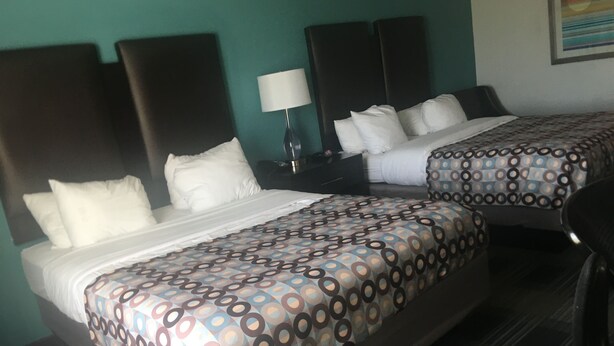A hotel room with two beds, each with a patterned bedspread, a nightstand with a lamp, and a painting on the wall. - Days Inn by Wyndham Alva (Alva)