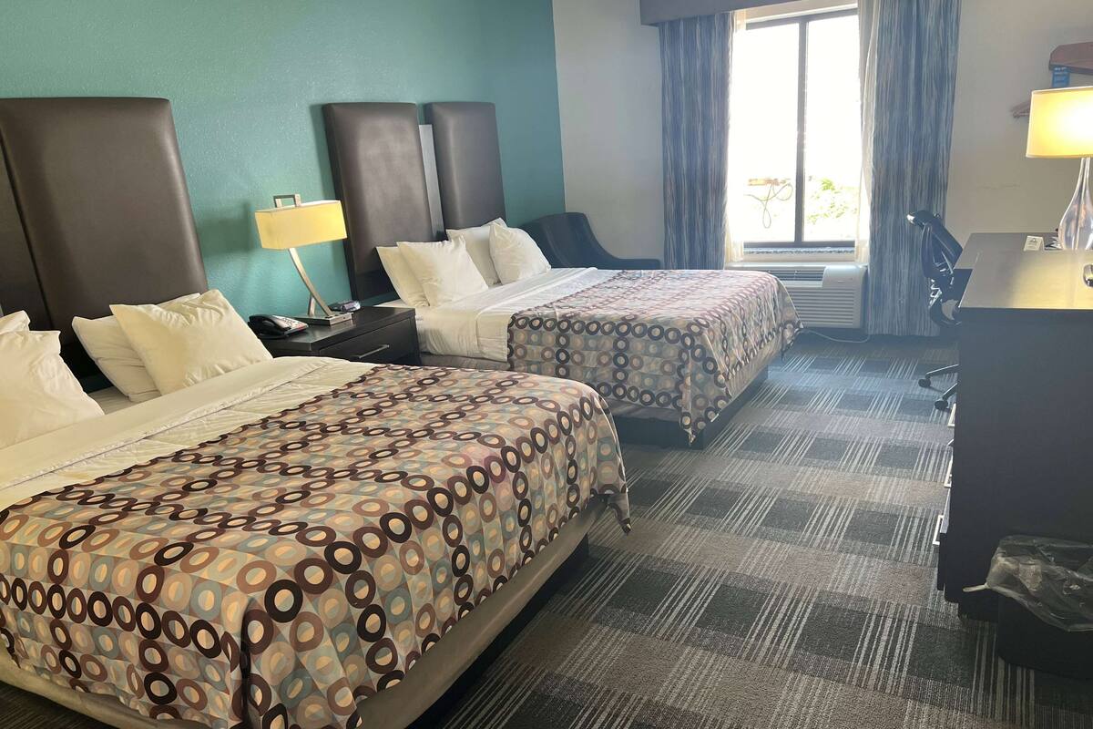 A hotel room with two beds, a desk, and a chair.