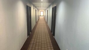 A long, narrow hallway with a patterned floor, doors on both sides, and a light at the end. - Days Inn by Wyndham Alva (Alva)