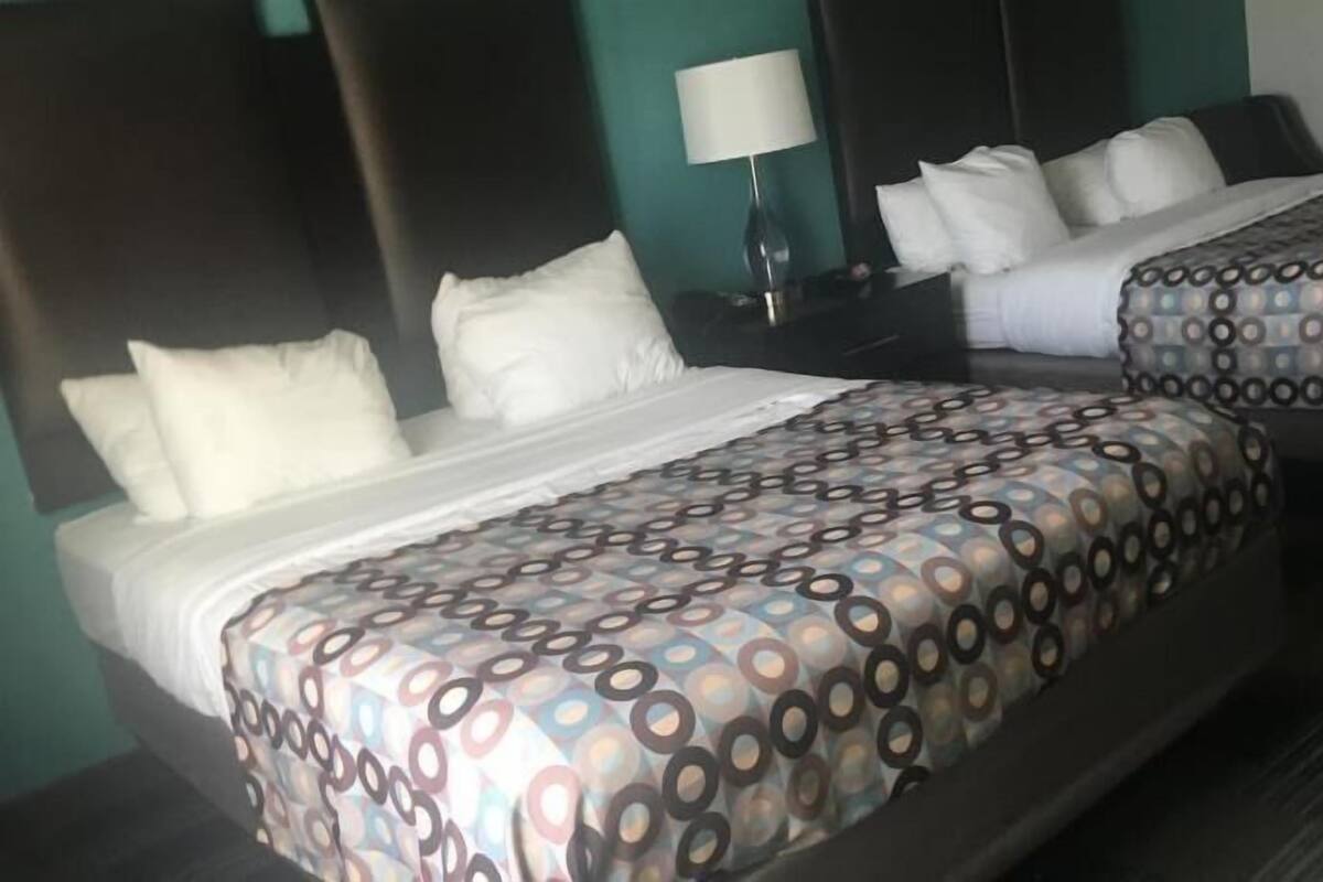 A hotel room with two beds, each with patterned bedding, a nightstand with a lamp, and a dark headboard.