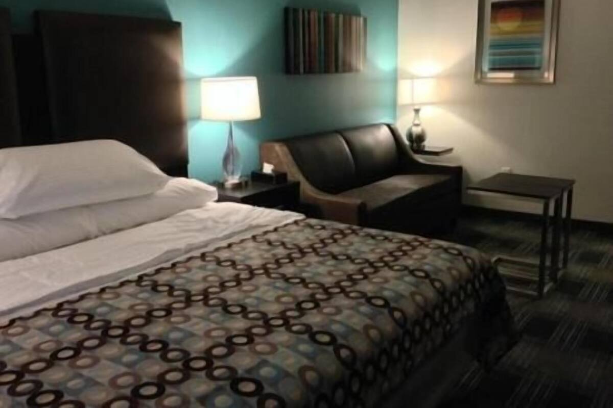 A hotel room with a bed, a chair, a nightstand, a lamp, and a painting on the wall.
