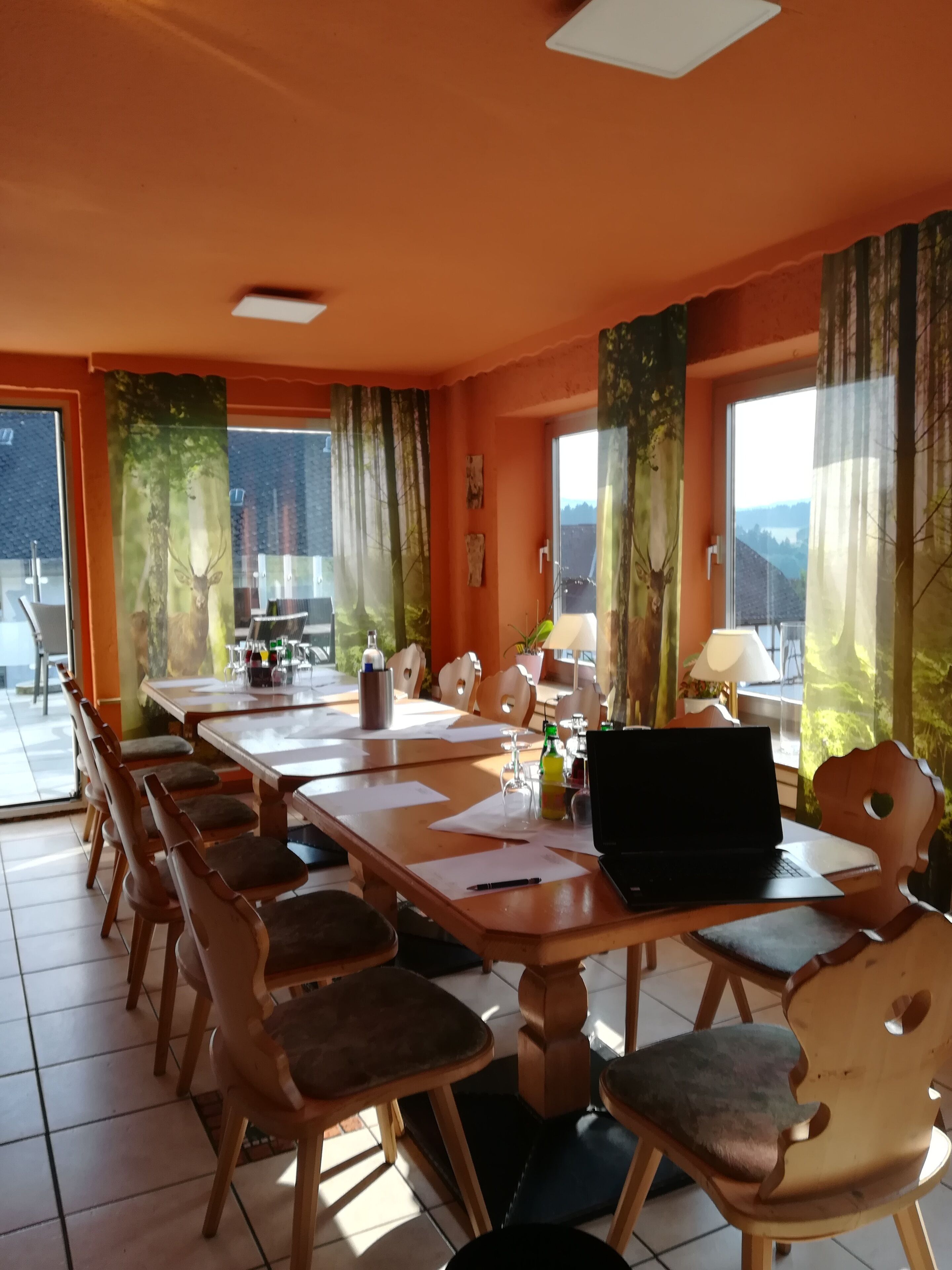 A dining area with a long table, chairs, a laptop, and a view of the outdoors.