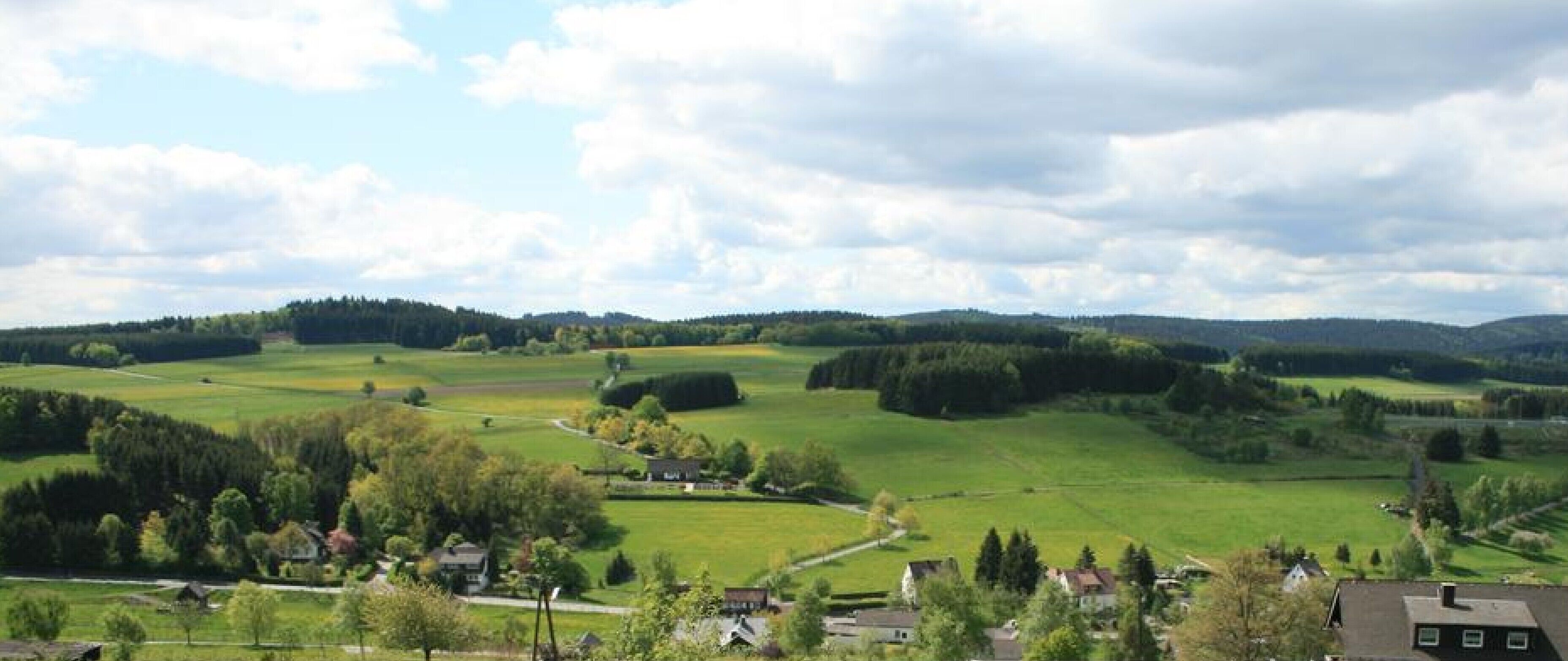 Paisagem rural com colinas ondulantes, casas espalhadas e céu limpo.