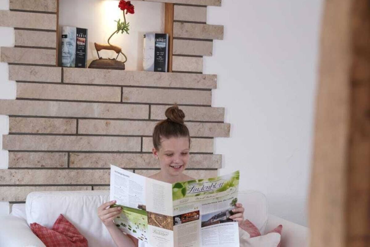 Une personne assise sur un canapé blanc, avec un livre, un vase de fleurs et une table en bois.
