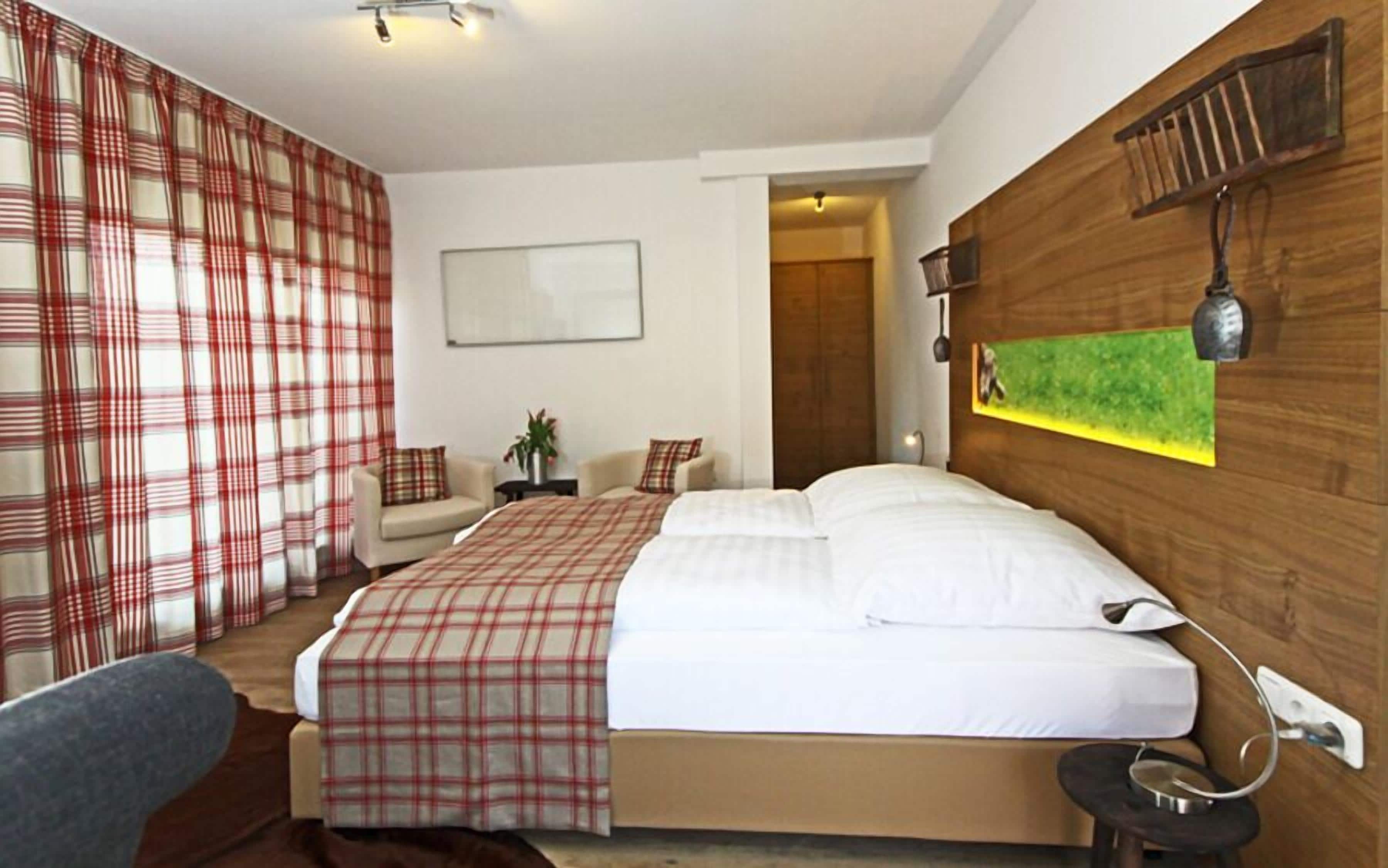 A hotel room with a large bed, a small sofa, a bedside table, and a wooden headboard.