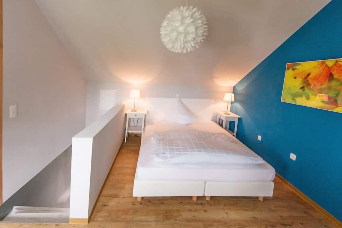 Une chambre à coucher avec un lit, des tables de chevet, un luminaire suspendu et un tableau au mur.