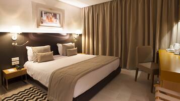 Habitación de hotel con una cama grande, un escritorio, una silla y una mesita de noche con lámpara.