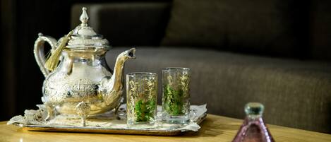 A silver teapot with a handle and spout, two glass cups with decorative patterns, and a small pink bottle on a wooden tray.