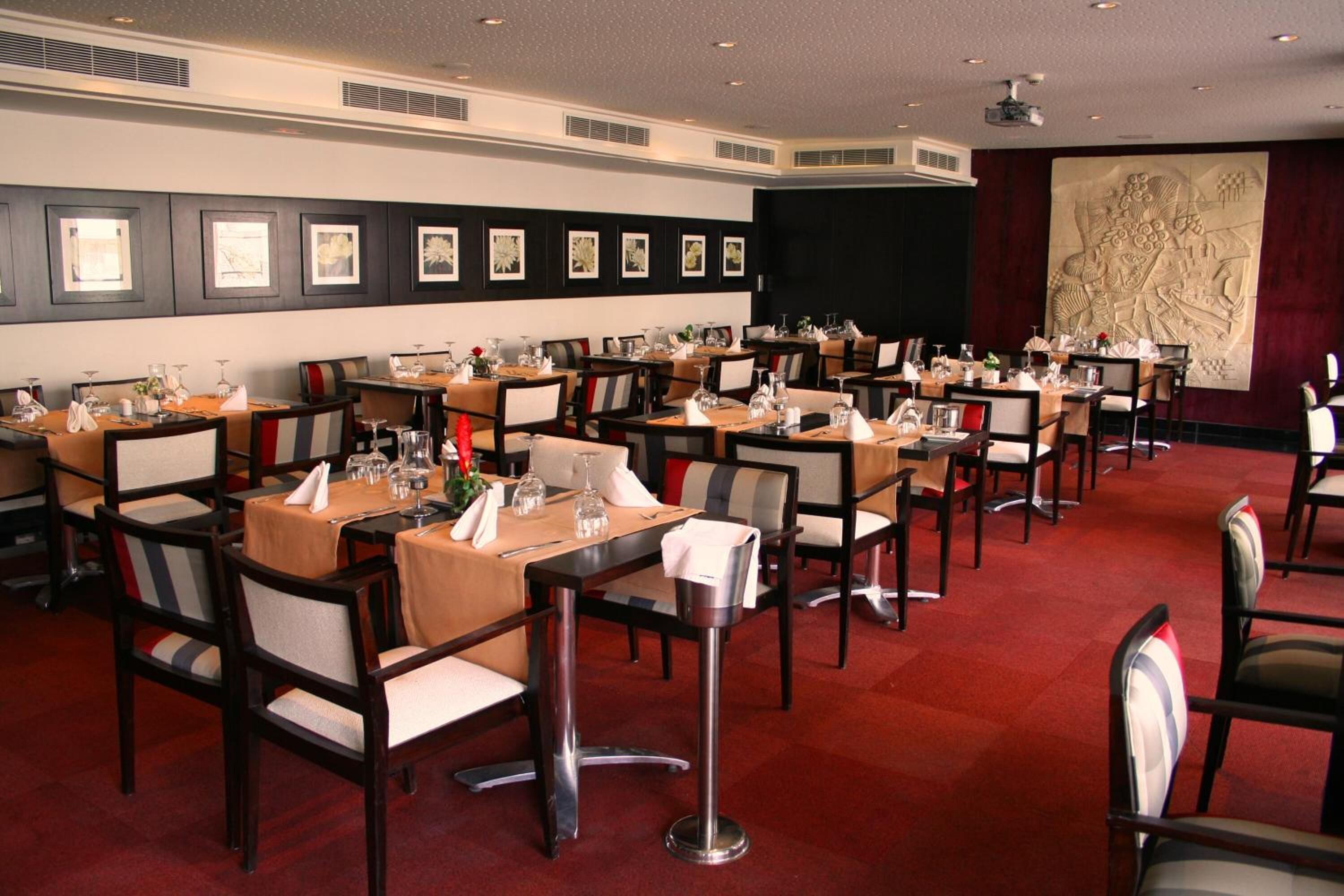 Un comedor formal con varias mesas y sillas, obras de arte enmarcadas en las paredes y un gran elemento decorativo en la pared.
