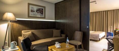 Una habitación de hotel moderna con sofá, una mesa de centro de madera, una silla, una cama y un escritorio con lámpara.