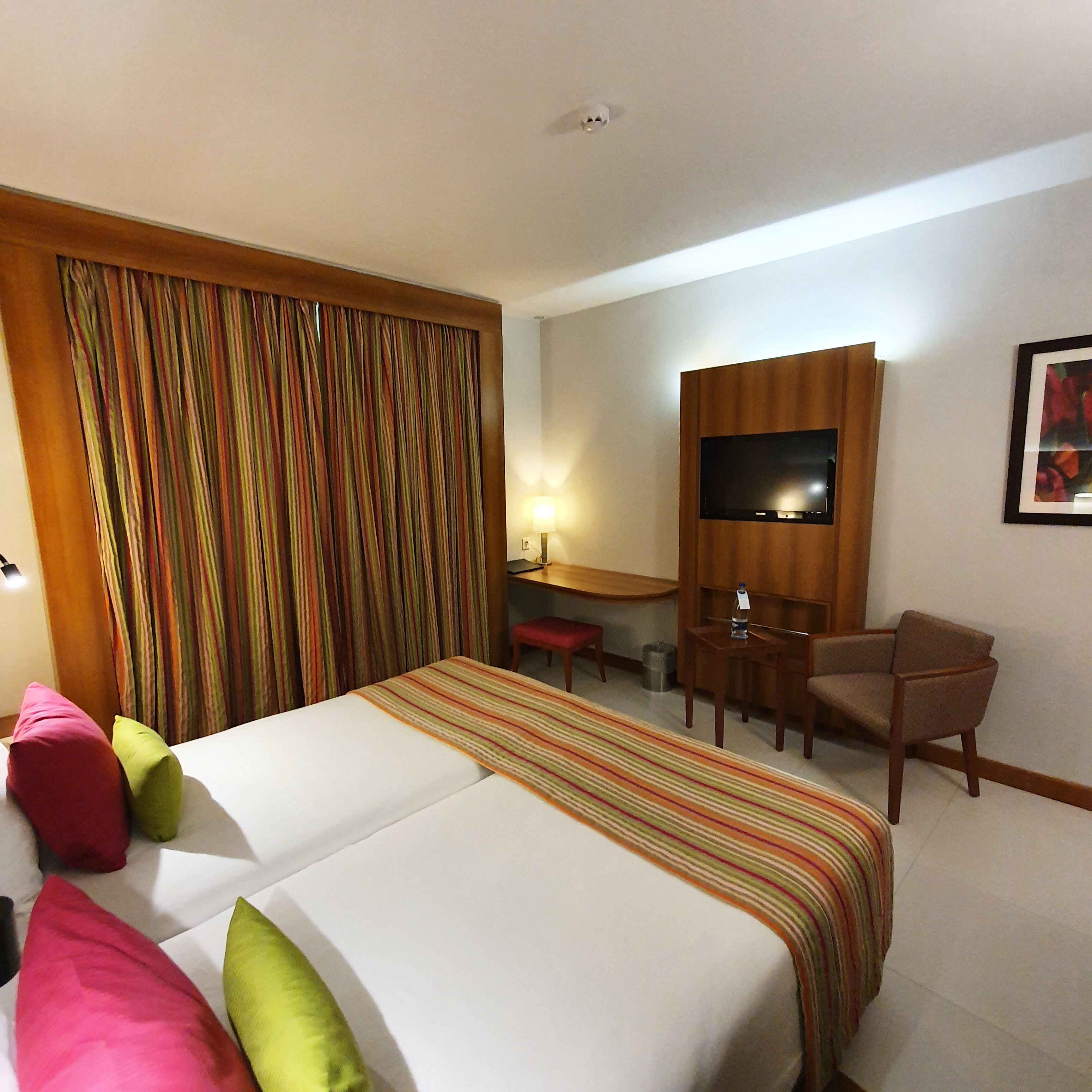 A hotel room with a bed, a desk, a chair, a television, and a curtain.